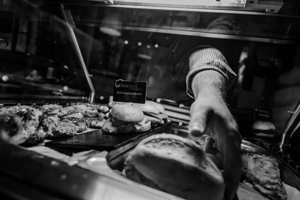 Mitarbeiter greift nach Schnitzelsandwich in der warmen Auslage, schwarz-weiß aufgenommen