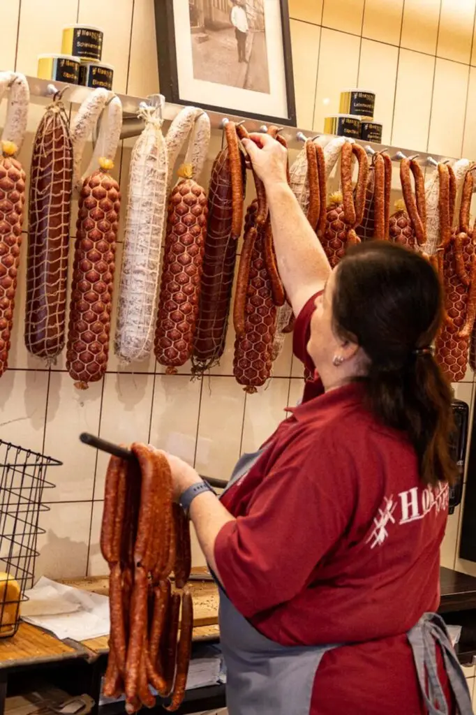 Mitarbeitende der Metzgerei Hornung in Bamberg hängt hausgemachte Wurstwaren im Verkaufsbereich auf