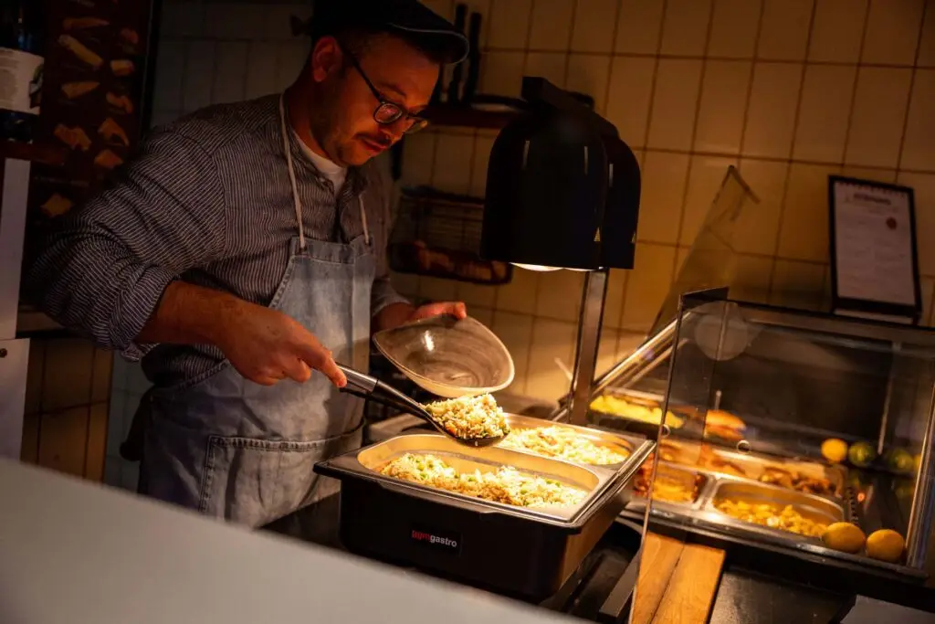 Mitarbeitender der Metzgerei Hornung Bamberg beim Anrichten eines Mittagsgerichtes an der warmen Theke