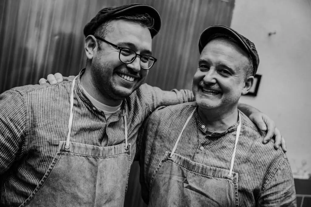 Zwei Mitarbeitende in Arbeitskleidung lachen gemeinsam in der Produktionsküche der Metzgerei Hornung in Bamberg