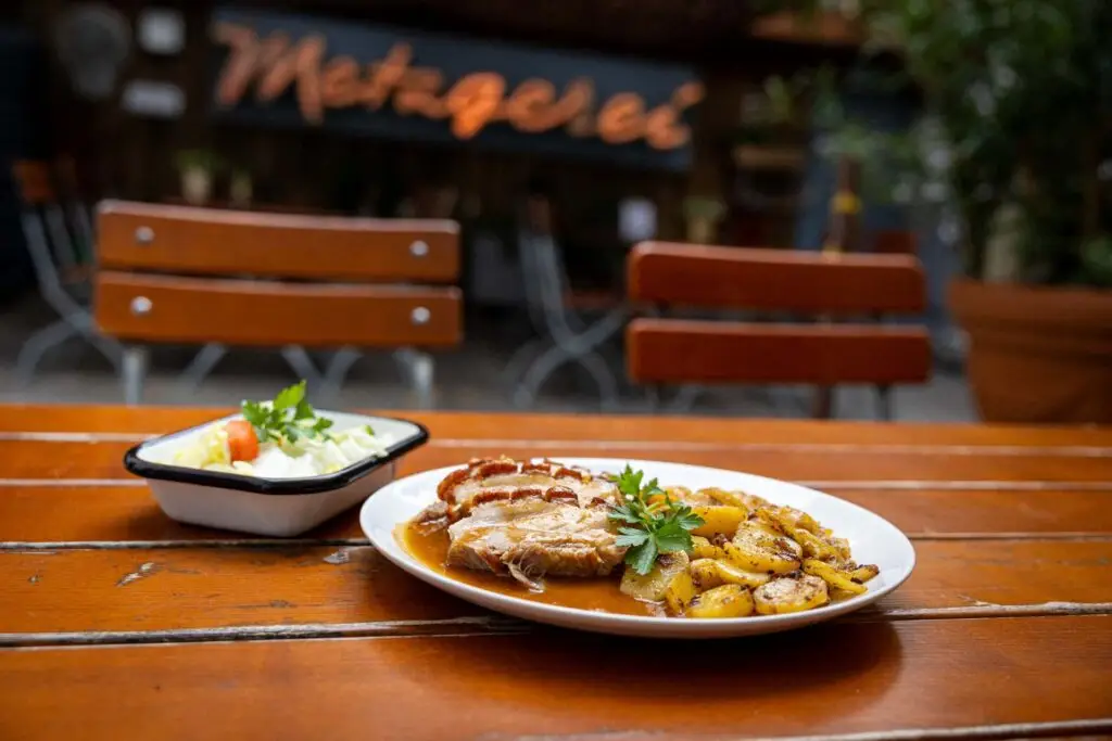 Mittagsgericht: Krustenbraten mit Bratkartoffeln und kleinem Salat schön platziert auf einem Tisch im Innenhof der Metzgerei Hornung Bamberg
