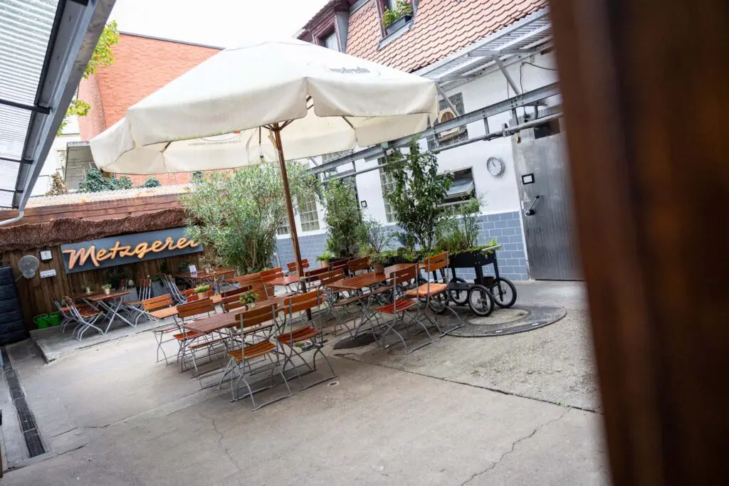 Sitzbereich im Innenhof der Metzgerei Hornung in Bamberg mit Biergartengarnituren und Sonnenschirm