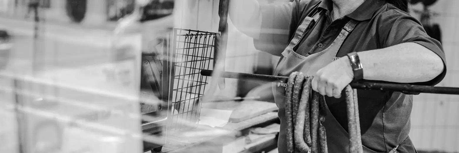 Schwarz-weiß Aufnahme einer Mitarbeiterin, die gerade frische Würste in die Theke der Metzgerei Hornung hängt.